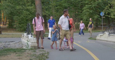 BUCHA/UKRAINE - JUL 19 2015: A family is on a holiday in a park, little girl drives a baby carriage, other people walk near, mid-shot, day, Ukraine.