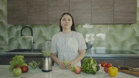 Young beautiful girl tells in kitchen how to make healthy smoothie from fruits and vegetables. Healthy eating ideas. Slow motion