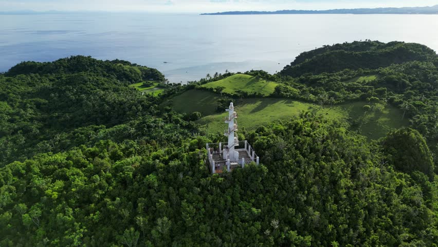 A stunning aerial shot circles and zooms in on the Boté Lighthouse perched atop a lush forestry hill, showcasing its historic beauty and coastal significance.
