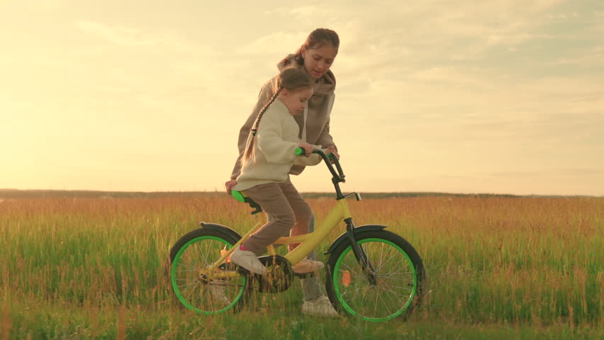 Young mother teaches child to keep balance while sitting on bicycle. Childhood dream to ride bike. Happy family life mom baby, Parental support. Mom teaches her little daughter to ride bicycle, sunset Royalty-Free Stock Footage #1101425529