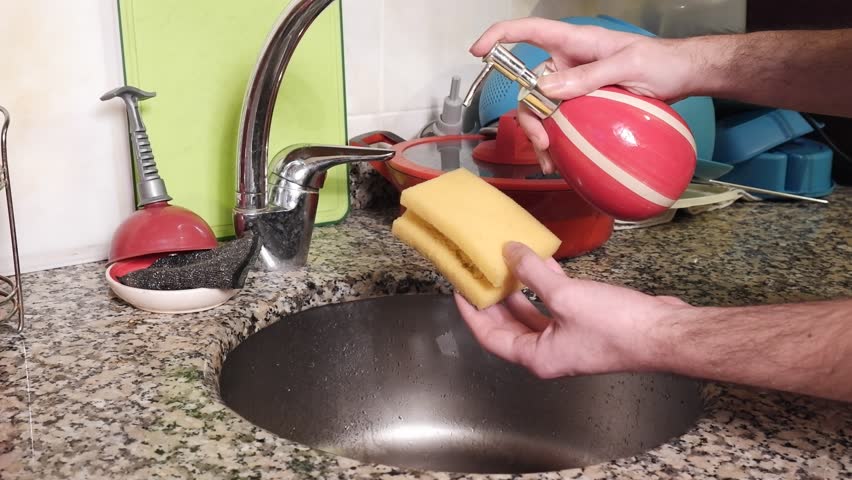 The man sprays dishwashing detergent from the ceramic soap dispenser on the yellow cleaning sponge in the messy kitchen. | Shutterstock HD Video #1101426145