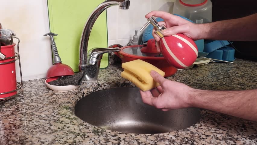 The man sprays dishwashing detergent from the china soap dispenser onto the yellow cleaning sponge and turns on the water to make the sponge foam. | Shutterstock HD Video #1101426147