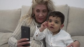 Video of a young autistic boy sitting with his blonde mother watching his cell phone and having fun on a video call.