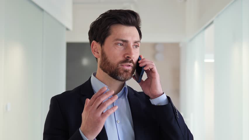 Confident and well dressed businessman who is multitasking by speaking on his mobile phone with a client. His ability to effectively manage his time is on full display, strong multitasking skills. Royalty-Free Stock Footage #1101435381