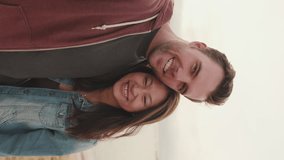 VERTICAL VIDEO: Couple in love hugging each other makes selfie while standing on the beach