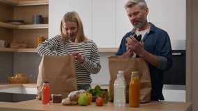 Caucasian middle-aged family adult mature couple wife and husband woman and man talking in kitchen unpack delivered paper bag with vegetables fruits sniffing apple talk food delivery online shopping - Powered by Shutterstock - Get 15% off with code: PIKWIZARD15