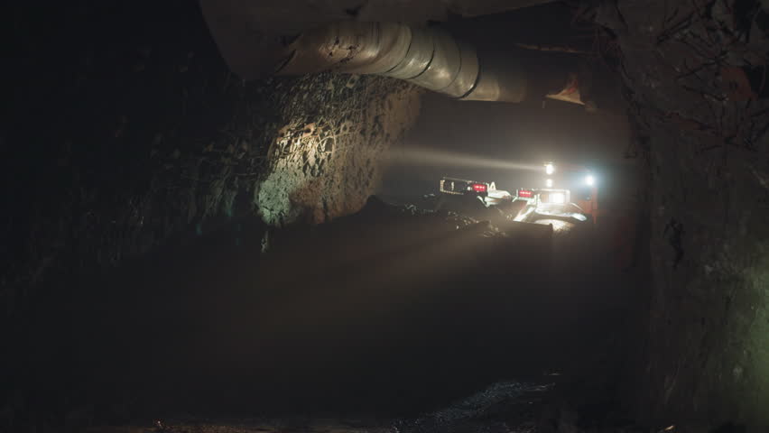 Mining machinery extracts and transports ore in dark mine illuminating area with bright lights. Heavy vehicle mines minerals with big dipper closeup