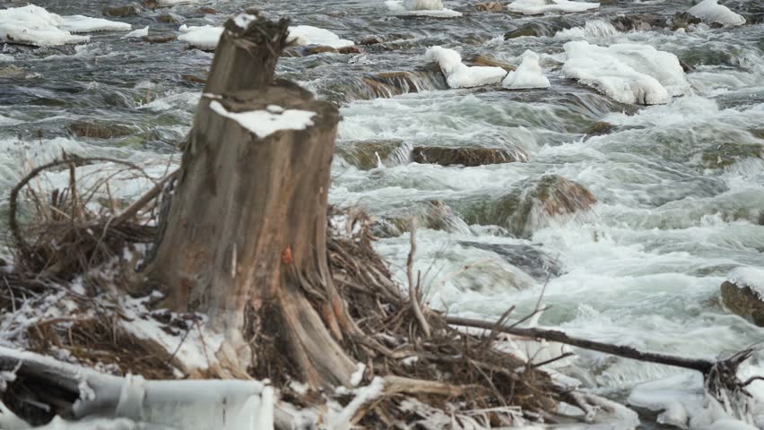 Winter river flowing near snow and ice covered stone cascade, closeup detail
