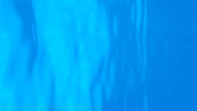 Vertical video, Underwater view on calm surface of blue water. Natural background with surface of blue water. Texture of blue water on surface. Close-up, Slow Motion