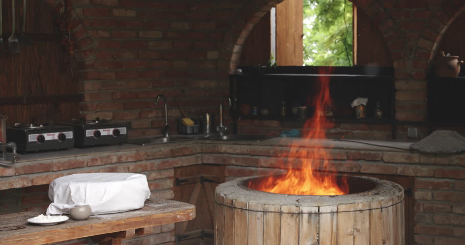 A Georgian Woman Baker Standing Next To The Round Stone Clay Oven With Burning Fire. Kakheti, Georgia - Medium Shot, Slow Motion