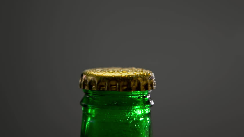 Cap of Full Beer Bottle Opens with Froth Smoke Close-up. Drink Alcohol Beverage in Modern Bar or Dark Pub to Quench Thirst. Aluminum Lid Top and Colorful Glass in Wet Condensation on Grey Background Royalty-Free Stock Footage #1101443543