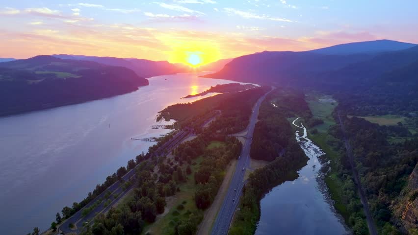 Aerial video captures the beauty of the Columbia River Gorge and Vista House-at sunrise-golden hour-the camera slowly tracks from left to right-from the river to behind the cliffs holding Vista House