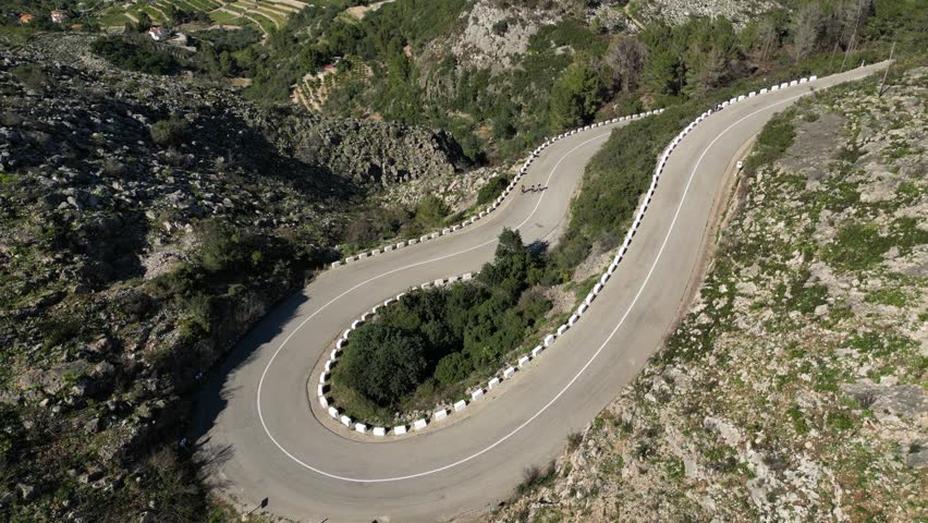 Aerial drone footage.Cyclist group in cycling kit and helmets conquering the Vall de Ebo pass in Spain.Cycling journey to the top.Сyclists ride on a winding road in the mountains.Pego,Alicante,Spain.