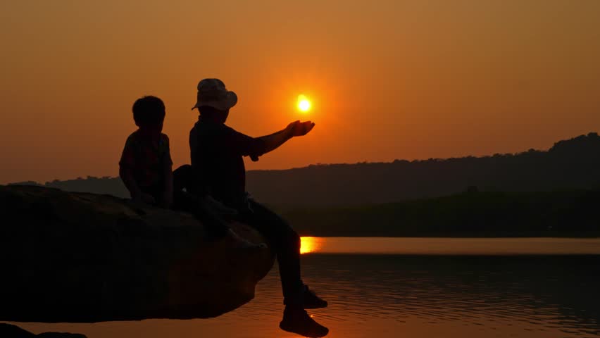 Tourist sitting on rocky cliff near river at sunset