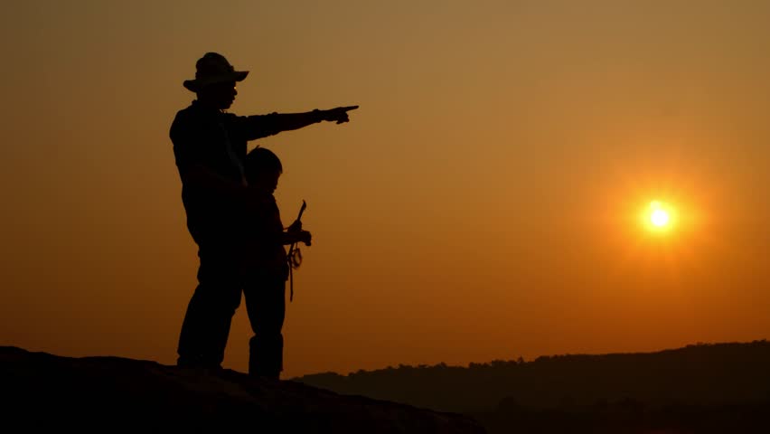 Tourist sitting on rocky cliff near river at sunset