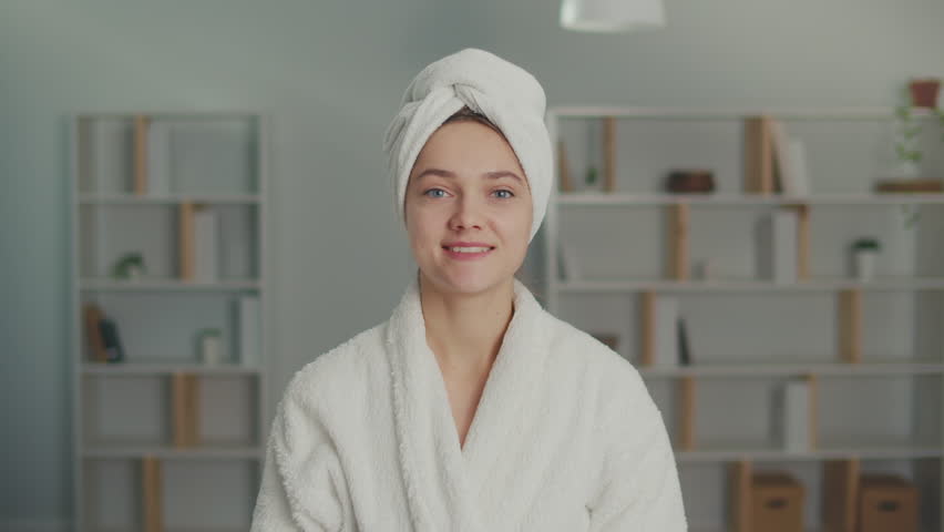 Portrait of a Smiling Young Woman Applying Moisturizing Cream on Her Face. A Happy Woman with a White Towel on Her Head Cares About Her Skin at Home. Concept of Skincare, Cosmetics, Healthcare. Royalty-Free Stock Footage #1101446683