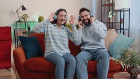 Happy overjoyed young family married couple man woman in wireless headphones dancing on couch at home listening favorite energetic disco rock n roll music. Husband and wife together weekend activities - Powered by Shutterstock - Get 15% off with code: PIKWIZARD15