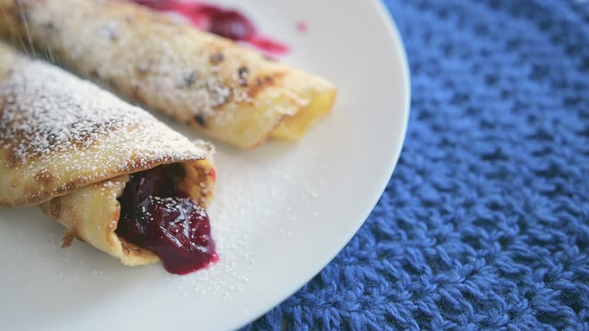 Homemade pancakes with preserved cherry jam, sprinkled with powdered sugar. Blue crochet napkin under the plate.  | Shutterstock HD Video #1101447307