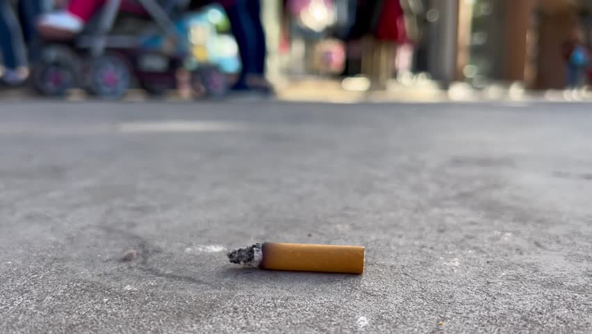 cigarette butt thrown on the street and people pass by looking at this inert garbage on the floor