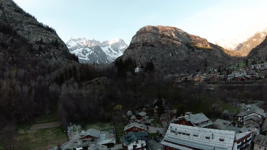 FPV drone aerial in alpine resort Courmayeur, Aosta Valley, Italy at foot of Alps Mont Blanc Monte Bianco, flying over houses and trees; winter; epic mountains panorama view; snowy mountain summits