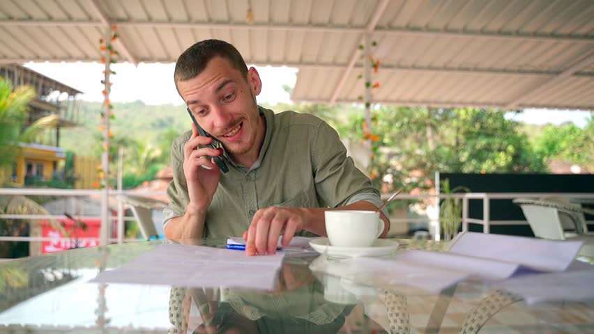 A young man talking on the phone, pointing his finger at a notebook.