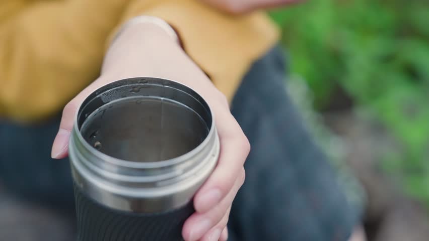 Young asian woman reading ebook with thermos in her hand. Pan up.
