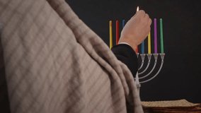 Orthodox jewish person light a hanukkah menorah colored candles on black background. - Powered by Shutterstock - Get 15% off with code: PIKWIZARD15