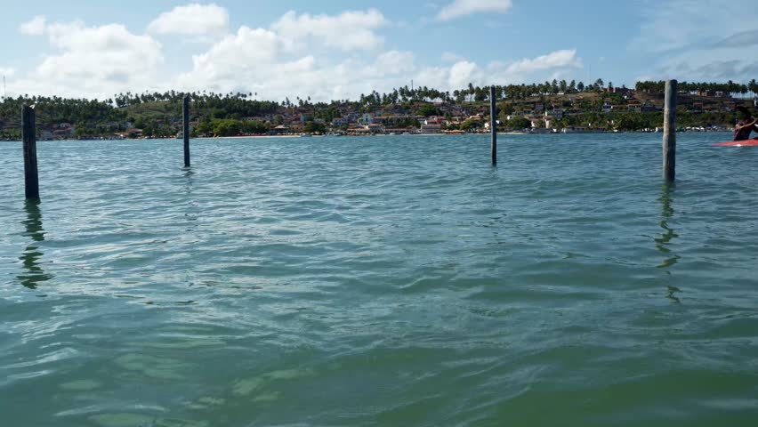 Tilt up shot from where the large tropical turquoise Curimataú river meets the sea from the Restinga beach across from the tropical coastal town of Barra do Cunhaú in Rio Grande do Norte, Brazil