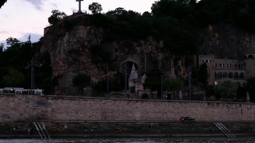 St. Gerard Sagredo Statue, Liberty Statue, Gellért Hill Cave, and Gellert Rock Chapel in Budapest, Hungary. Danube River, golden hour clouds in sky, bluffs, cliffs - smooth cinematic 4k 30fps footage