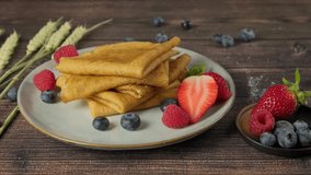 Person taking a plate with French crepes served on plate with fresh berries, woman's hands grabbing folded pancakes from table, side view video clip, high quality 4k footage