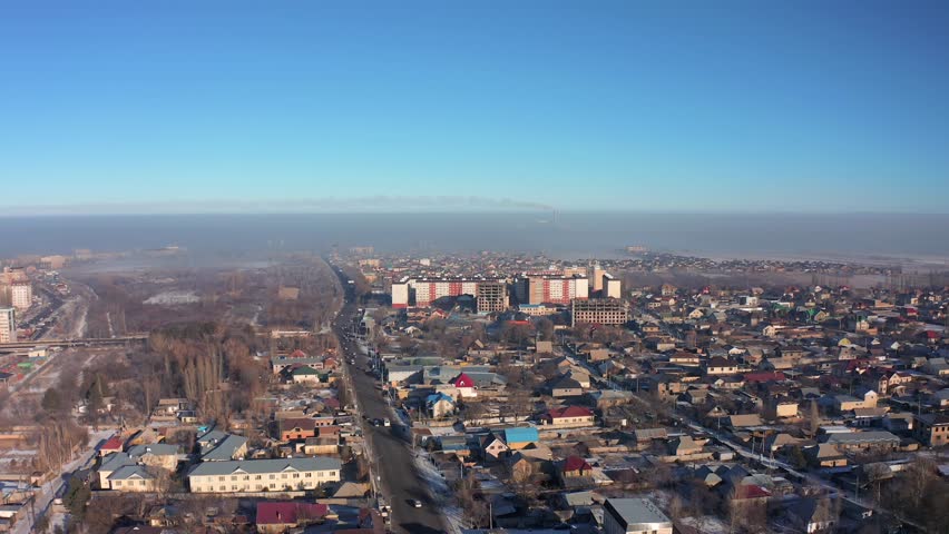Flying forward directly over the houses in the suburbs of the most polluted city in the world Bishkek against the backdrop of a city covered in smog and smoke, an ecological disaster