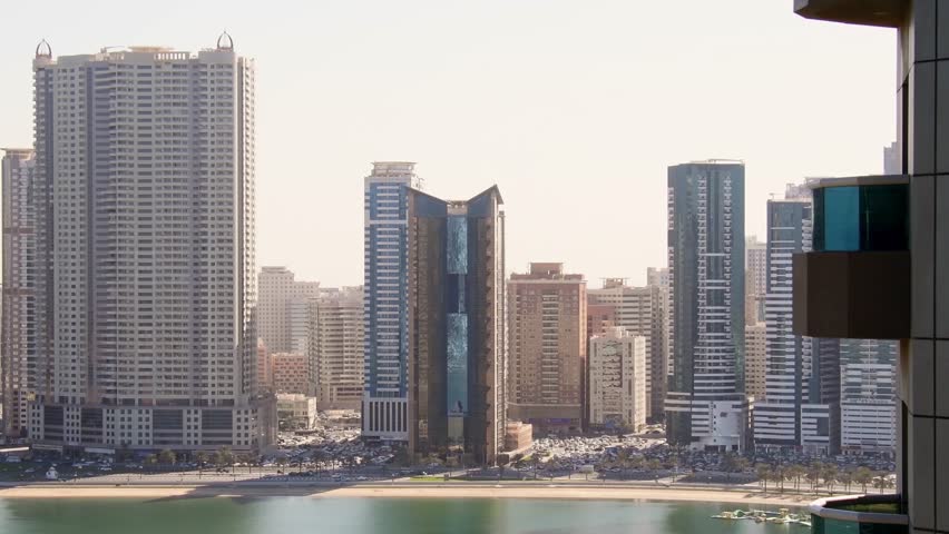 Panoramic window view to high buildings with balconies and marina in Sharjah district. Rented apartment stunning views and real estate business in united arab emirates