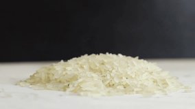 Rice grains spill out of a plastic white scoop, close-up. Rice long parboiled polished. Grains of rice fall into a pile on a black background