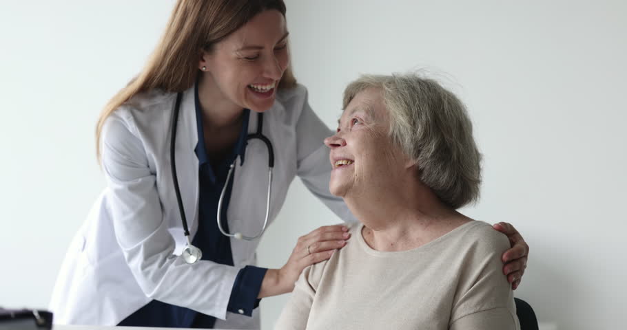 Positive caring physician doctor giving medical support, healthcare help, consultation to old patient, touching shoulders, hugging elderly 80s woman, smiling, laughing, talking Royalty-Free Stock Footage #1101476227