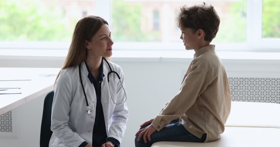 Engaged caring pretty female pediatrician with stethoscope talking to little patient boy, asking about complaints, speaking, smiling, laughing, examining child in doctor office | Shutterstock HD Video #1101476257