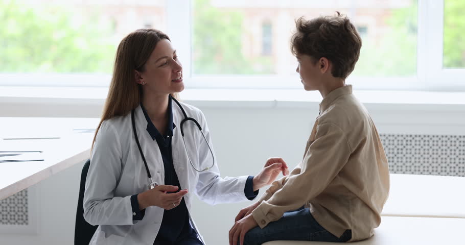 Engaged caring pretty female pediatrician with stethoscope talking to little patient boy, asking about complaints, speaking, smiling, laughing, examining child in doctor office | Shutterstock HD Video #1101476257