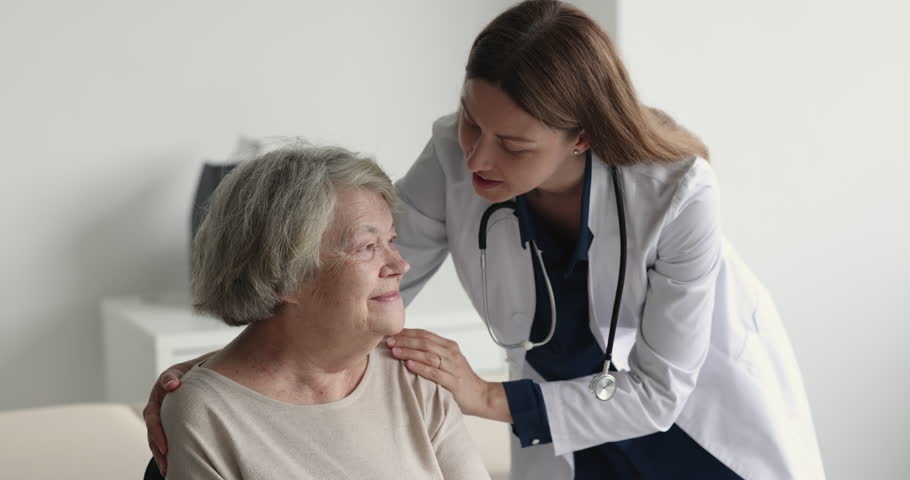 Empathetic geriatric doctor calming down positive smiling senior patient, touching shoulders, hugging, talking to elderly woman in physician office, speaking, explaining treatment details Royalty-Free Stock Footage #1101476269