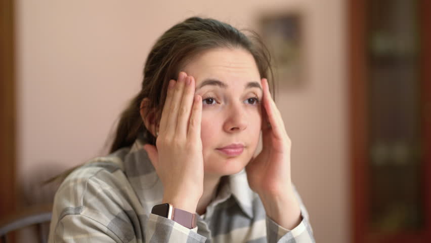 Headache from work fatigue. Portrait unhappy young woman sits and holds her head with her hands.