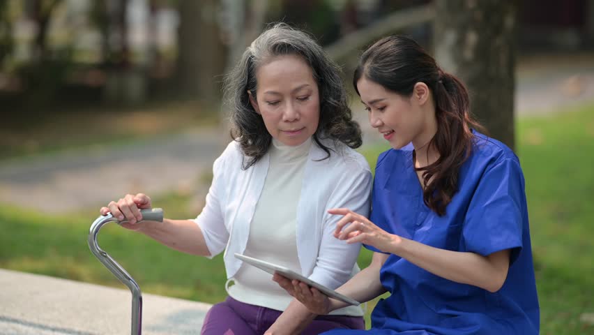 Delighted doctor in uniform pointing on digital tablet and showing medical reports to elderly woman at outdoor nursing home Royalty-Free Stock Footage #1101479029