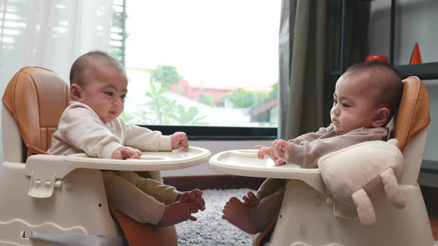 Asian twin babies sitting on safety chair, the chair can use for car seats, Two little baby waiting to eat at home