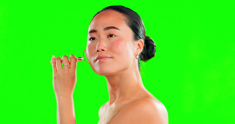 Beauty skincare, face and Asian woman with roller on green screen in studio isolated on a background mockup. Dermatology, massage and happy female model with rose quartz for facial skin treatment. | Shutterstock HD Video #1101484107
