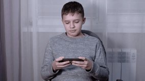 Handsome boy talking on a smartphone online in Room. Smiling teenager communicates on a mobile phone with friends, and parents, sitting in an armchair. Online education, video communication, internet.
