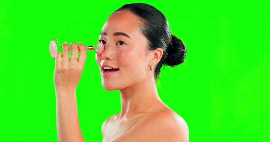 Face, beauty skincare and Asian woman with roller on green screen in studio isolated on a background mockup. Dermatology, facial and happy female model with rose quartz stone for skin treatment. | Shutterstock HD Video #1101488617