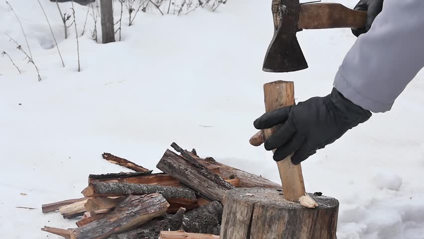 a hand in a black glove with an ax cannot cut a log in a snowy yard, slow motion.