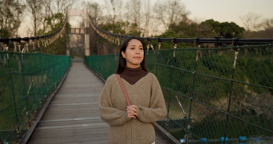 Woman walk along with the suspension bridge under sunset
