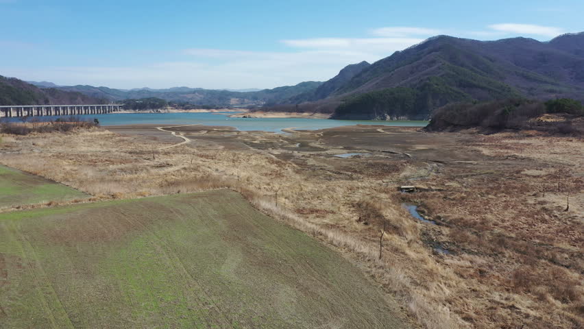 Aerial view of dry grasses and mud flats of lake in valley under blue sky.