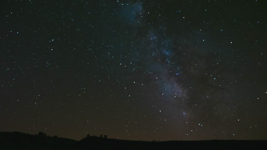 A starry sky with the milky way over the silhouette of a hill. Aeroplane lights fly quickly across the sky. A timelapse of a clear starry sky. A smooth zoom out with the camera