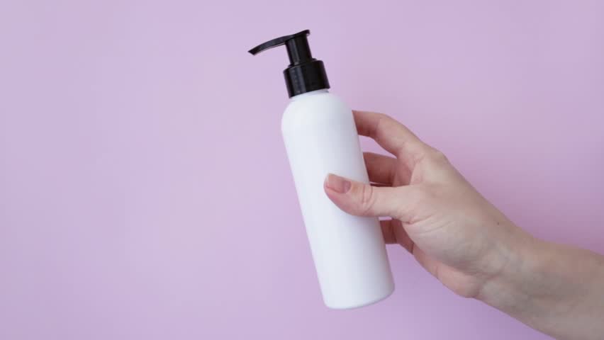 Female hand holding dispenser bottle with shampoo conditioner or cream shower gel on pink background | Shutterstock HD Video #1101498049