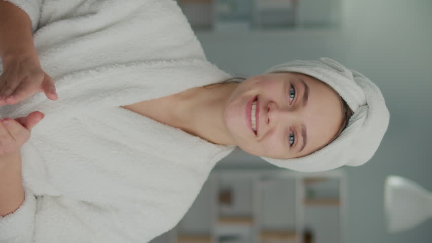 Vertical View. Portrait of a Smiling Young Woman Applying Cream on Her Face. A Happy Woman with a White Towel on Her Head Cares About Her Skin at Home. Concept of Beauty and Health. | Shutterstock HD Video #1101498405