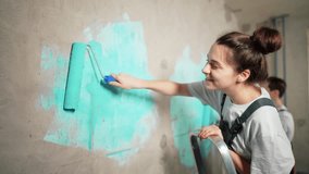 Happy family couple together painting and priming wall with painting roller. House painters working. Home renovation process in new building after moving. Stages of preparing wall for wallpapering. - Powered by Shutterstock - Get 15% off with code: PIKWIZARD15